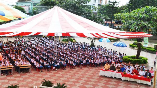 Khách mời và học sinh ngồi dưới bóng mát của những chiếc dù